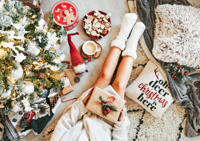 Overhead lifestyle photo of woman in sweater sitting by christmas tree. opening presents.