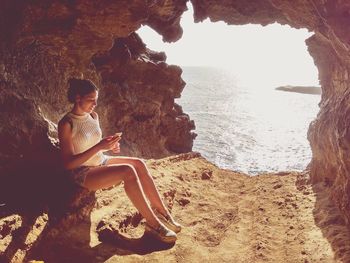 Woman using mobile phone while sitting on rock in cave