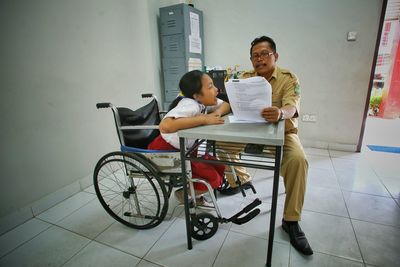 Police officer reading document by disabled girl on wheelchair in school office