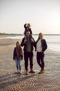 Family in a leather jacket walks along the beach with their dog in autumn