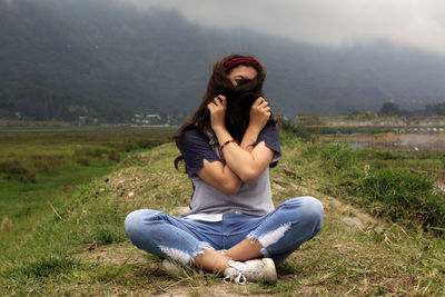 Young woman sitting on land and hide her face with long hair.