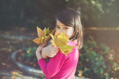 Happy mixed race japanese girl in autumn park holding maple leaves, smiling. sunlight, copy space