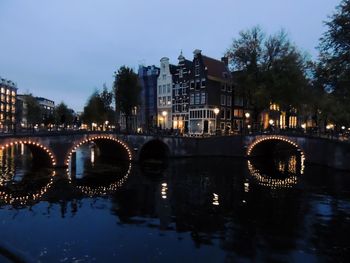 Illuminated bridge over river against sky at night