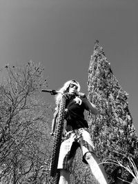 Low angle view of woman with arms raised against clear sky