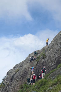 Low angle view of people standing on rocky mountain against sky