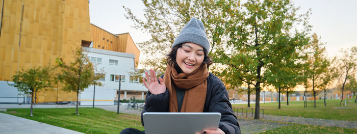 Portrait of young woman using mobile phone while standing against trees