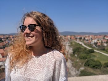 Young woman wearing sunglasses standing against clear blue sky