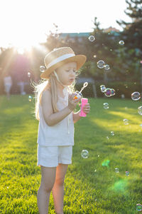 Full length of girl blowing bubbles while standing at park