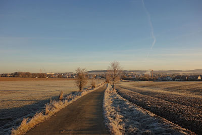 Road amidst field against sky during winter