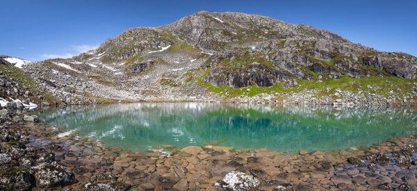 Scenic view of lake by mountain against blue sky