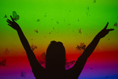 Rear view of silhouette woman with arms outstretched standing at sunset