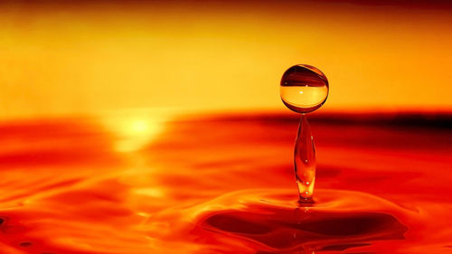 Close-up of water drop on glass against orange sky