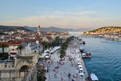 High angle view of people on footpath by river against sky in city during sunset