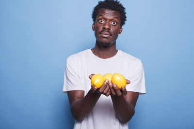 Portrait of young woman holding apple against blue background