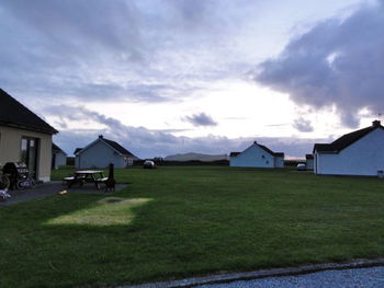 Houses on grassy field against cloudy sky