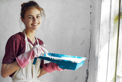 Portrait of young woman using mobile phone while standing against wall