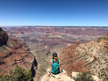 Woman sitting on rock against clear blue sky