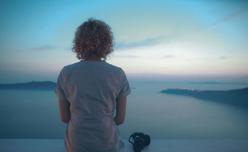 Rear view of woman sitting on retaining wall against sea