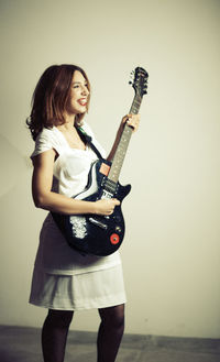 Full length of woman holding guitar against wall