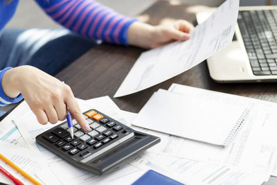 Midsection of woman using calculator while working on table