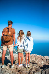 Rear view of friends standing on rock by sea against blue sky