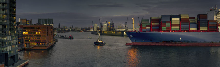 Boats on river by city against sky at dusk