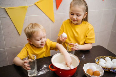 Girl breaks an egg into dough, brother helps cook, easter holiday