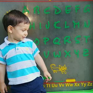 Boy standing against alphabets on blackboard