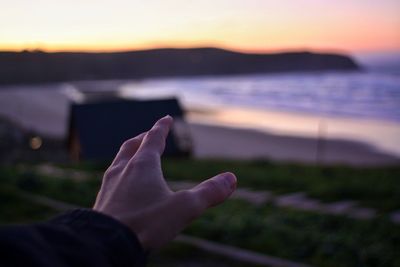 Cropped hand gesturing against beach during sunset