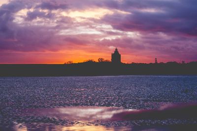 Silhouette of lighthouse at seaside during sunset