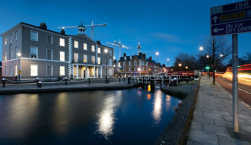 Canal by illuminated buildings in city at night