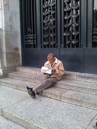 Senior man reading newspaper while sitting on steps by door