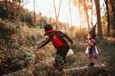 Girl wearing witch hat standing with brother at forest during halloween