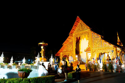 People at illuminated temple outside building at night