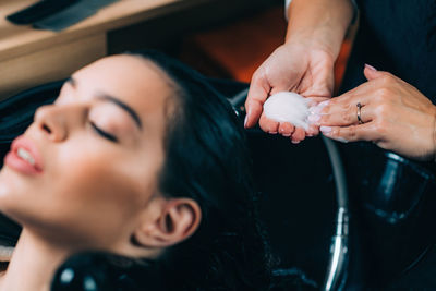 Midsection of hairdresser applying shampoo on woman hair in salon