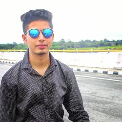 Portrait of young man wearing sunglasses standing against sky