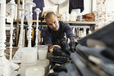 Male owner arranging jeans on table by candles at clothing store