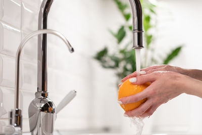 Female washing orange fruit in fresh water from kitchen sink crane. hygiene, healthcare and safety