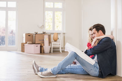 Young couple in new home sitting on floor looking at ground plan