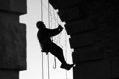 Low angle view of silhouette man hanging by building