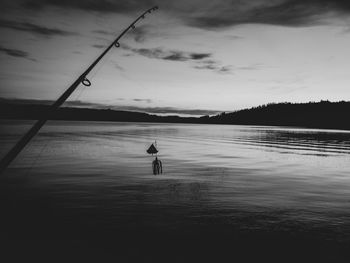 Silhouette man fishing in lake against sky