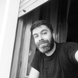 Portrait of young man standing against window at home