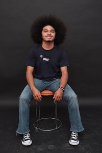 Man with frizzy curly hair, wearing a black t-shirt and jeans and shoes