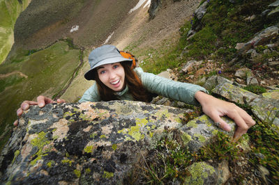 Happy woman climbs a rock while trekking outdoors. carefree backpacker smiling at camera