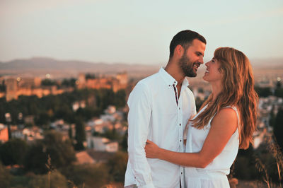 Smiling couple standing against cityscape during sunset