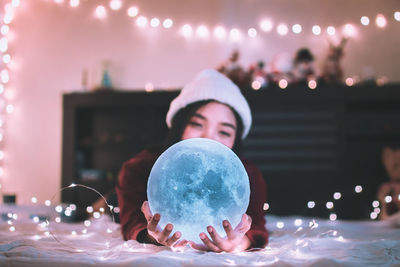 Young woman with illuminated ball and string lights at home