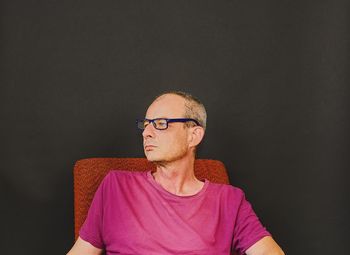 Thoughtful mature man sitting on chair against black wall