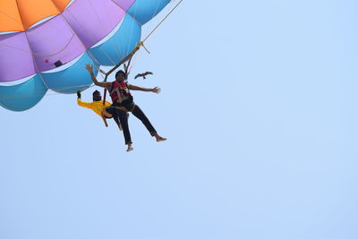 Low angle view of men flying against clear blue sky