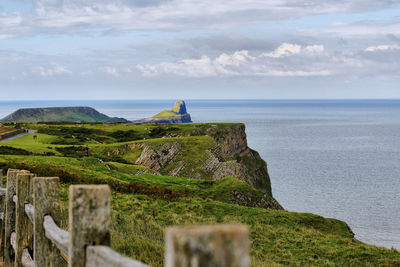 Scenic view of cliff by sea against cloudy sky