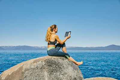 Man using mobile phone while sitting on rock against sea